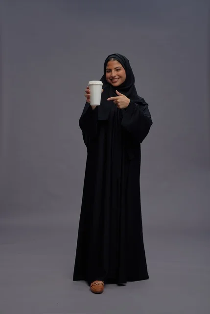 امرأة سعودية بعباءة سوداء تحمل كوب قهوة في الاستوديو
