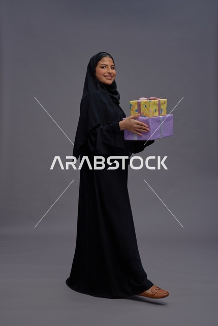امرأة سعودية بالعباءة السوداء تحمل علب هدايا