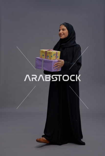 امرأة سعودية بالعباءة تحمل صناديق هدايا ملونة