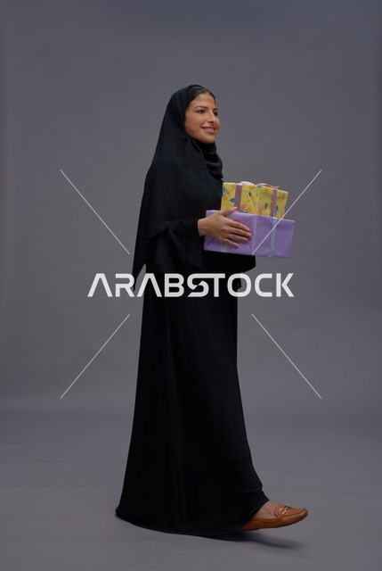 امرأة سعودية بالعباءة السوداء تحمل صناديق هدايا