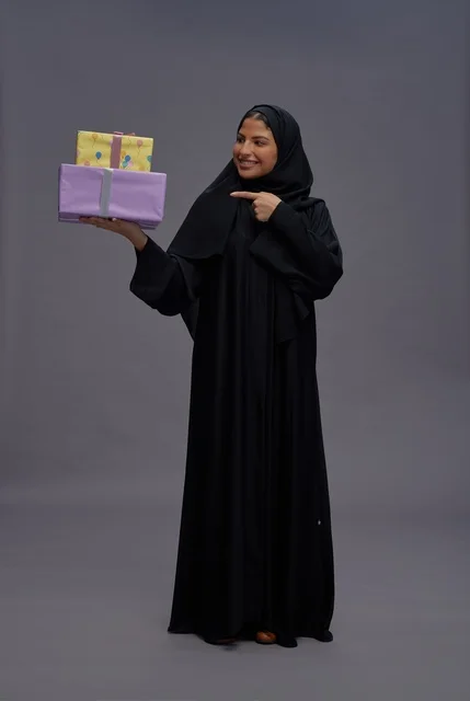 امرأة سعودية بعباية سوداء تحمل علب هدايا