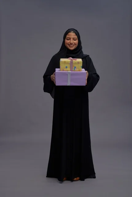 امرأة سعودية بعباية سوداء تحمل صناديق هدايا احتفالية