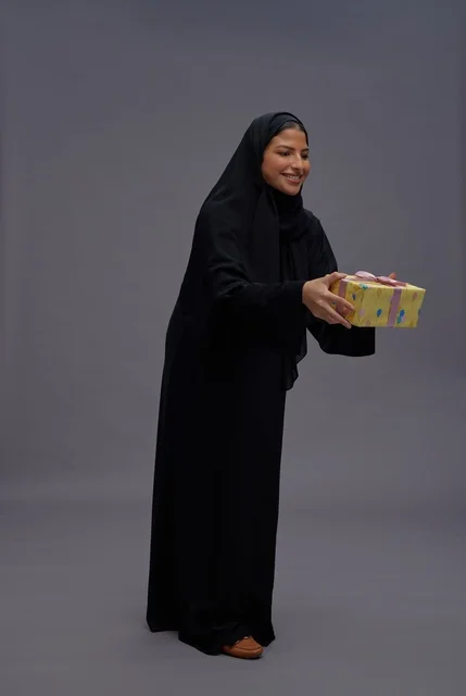 امرأة سعودية بعباية سوداء تحمل صندوق هدايا أصفر