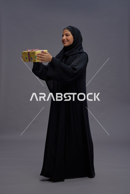 امرأة سعودية بعباءة سوداء تحمل علبة هدية