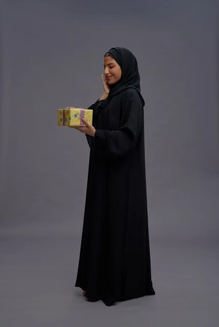 امرأة سعودية بعباية سوداء تحمل علبة هدية صفراء