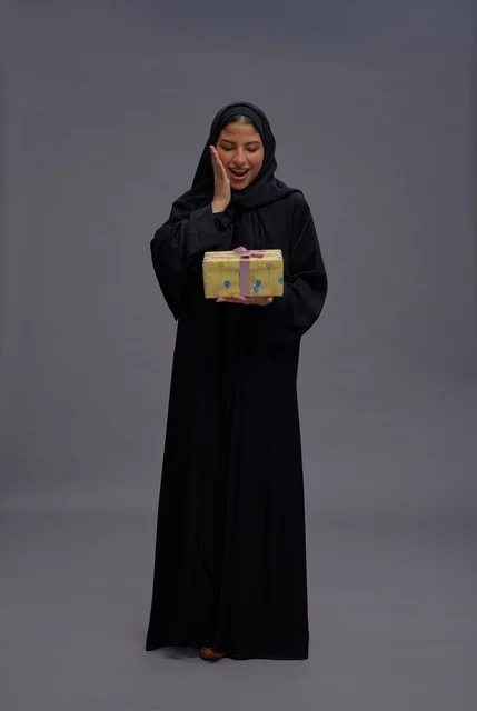 امرأة سعودية بعباية سوداء تحمل علبة هدية في استوديو امرأة سعودية بعباية سوداء تحمل علبة هدية في استوديو