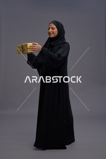 امرأة سعودية بالعباية تحمل علبة هدية صفراء