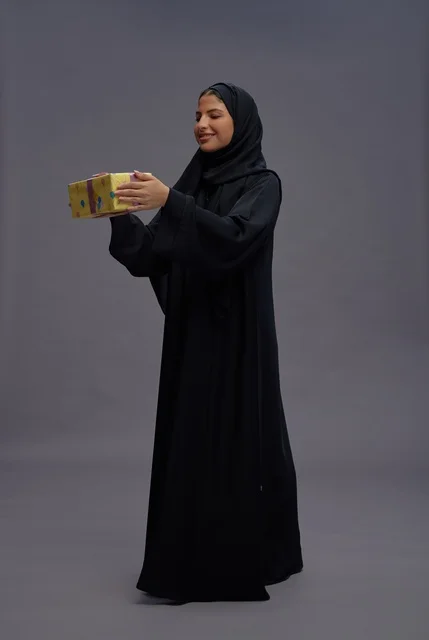امرأة سعودية بالعباية تحمل علبة هدية صفراء