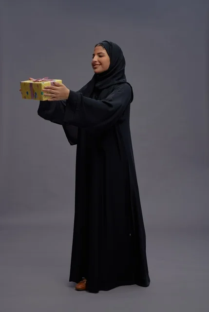 امرأة سعودية بعباية سوداء تحمل علبة هدية امرأة سعودية بعباية سوداء تحمل علبة هدية