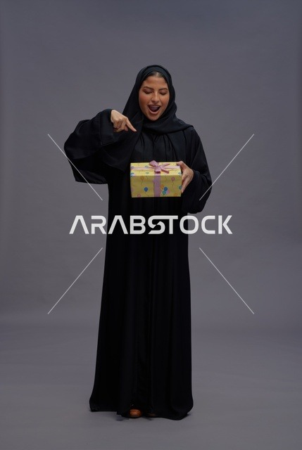 امرأة سعودية بعباية سوداء تحمل علبة هدية صفراء