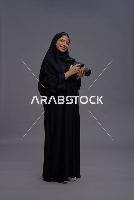 امرأة سعودية بعباية تمسك كاميرا احترافية