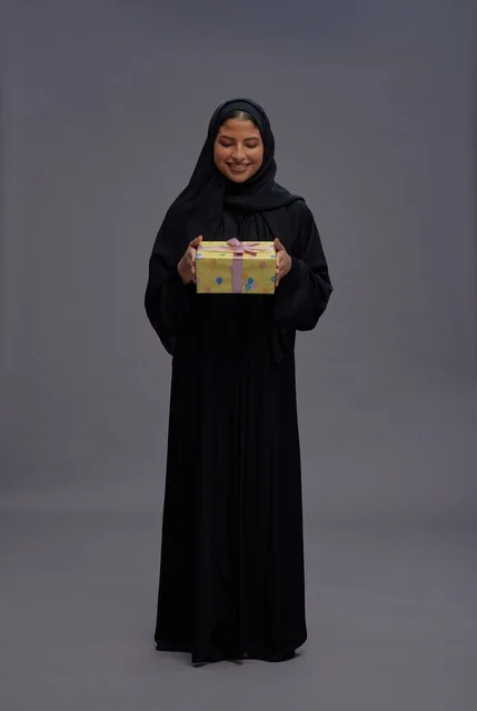 امرأة سعودية بعباية سوداء تحمل علبة هدية في استوديو