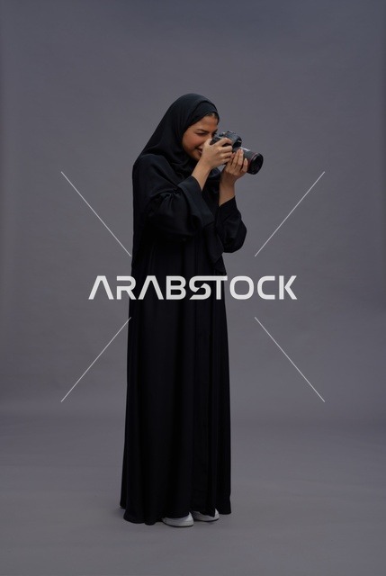 امرأة سعودية بالعباية تمسك كاميرا احترافية في استوديو