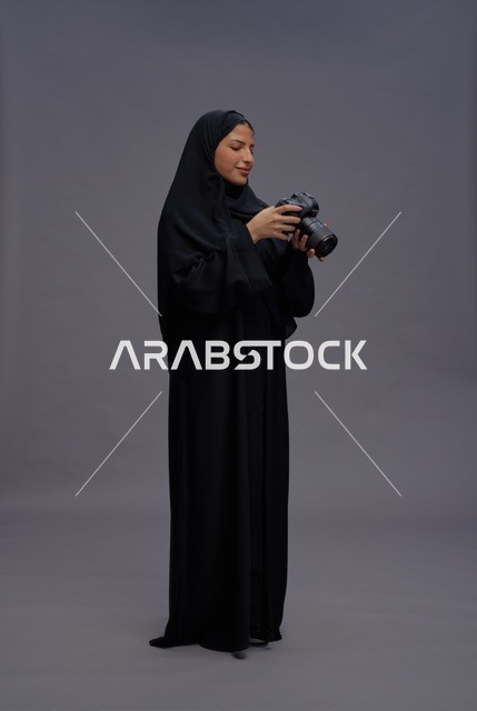 امرأة سعودية بالعباءة تمسك بكاميرا احترافية في استوديو