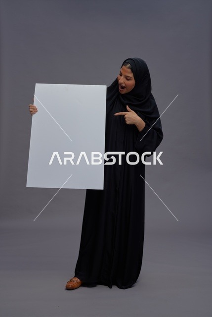 امرأة سعودية بعباءة سوداء تحمل لوحة بيضاء