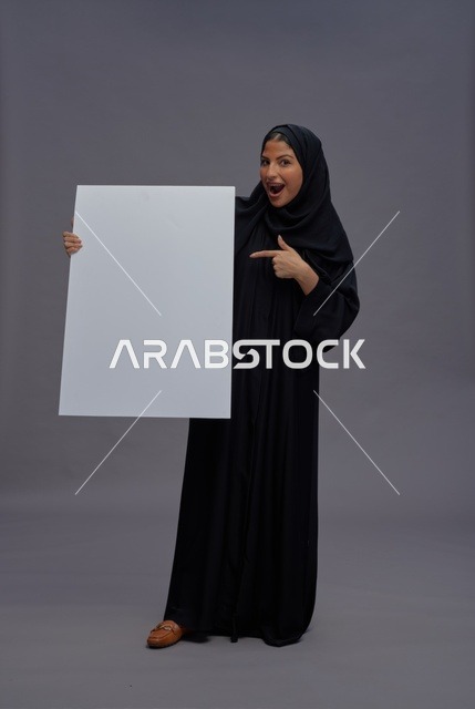 امرأة سعودية بالعباية السوداء تحمل لوحة بيضاء فارغة