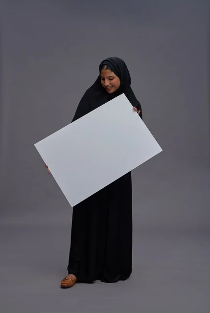 امرأة سعودية بعباية سوداء تحمل لوحة بيضاء فارغة