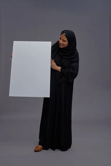 امرأة سعودية بالعباءة السوداء تحمل لوحة بيضاء فارغة