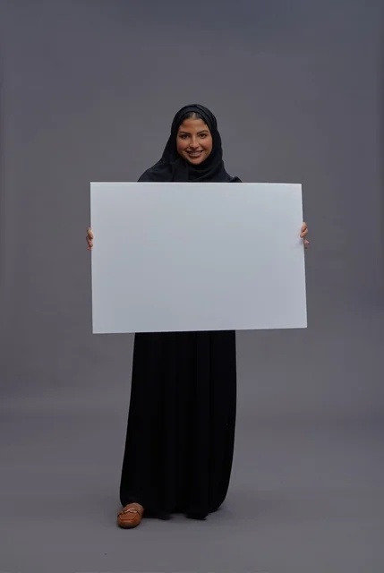 امرأة سعودية بالعباءة السوداء تحمل لوحة بيضاء