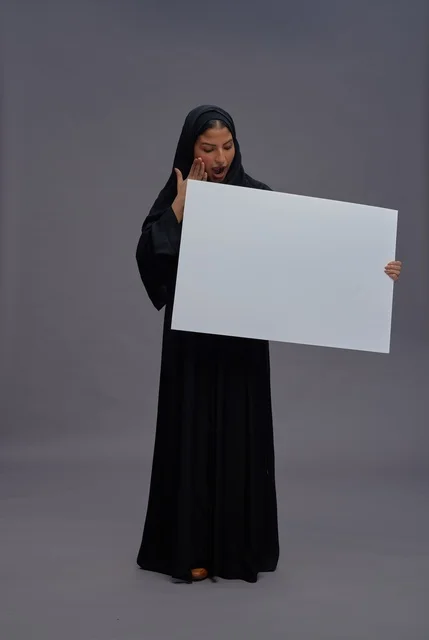 امرأة سعودية بعباية سوداء تحمل لوحة بيضاء فارغة