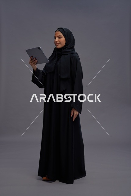 امرأة سعودية بالعباءة تستخدم جهاز لوحي خلفية رمادية