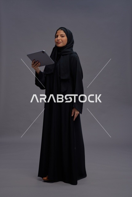 امرأة سعودية بالعباءة السوداء تستخدم جهازاً لوحياً