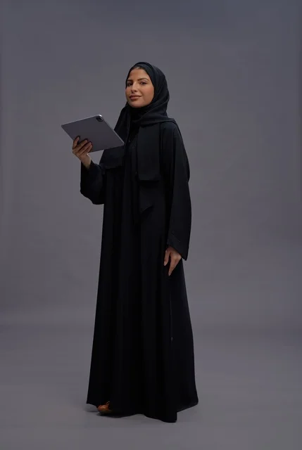 امرأة سعودية بالعباءة السوداء تستخدم جهازاً لوحياً