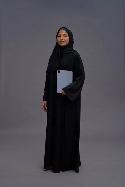 امرأة سعودية ترتدي العباءة وتحمل جهازاً لوحياً في الاستوديو