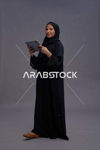 امرأة سعودية بعباءة سوداء تستخدم جهازاً لوحياً