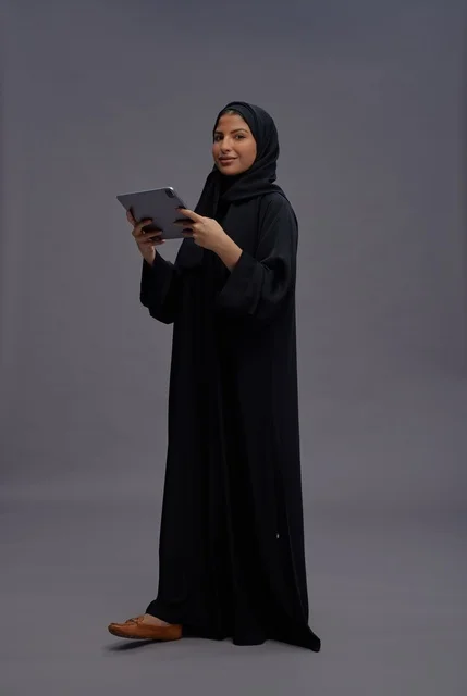 امرأة سعودية بعباءة سوداء تستخدم جهازاً لوحياً
