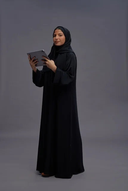 امرأة سعودية بالعباءة تستخدم جهازاً لوحياً في الاستوديو
