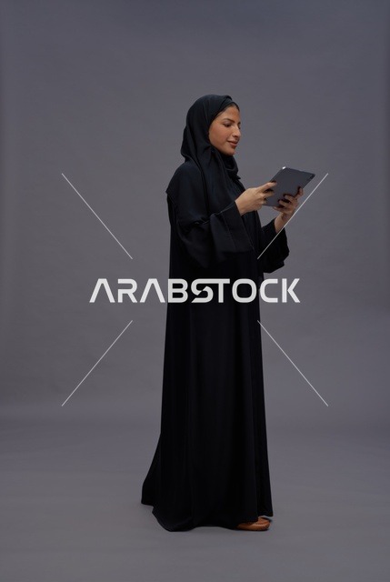 امرأة سعودية بالعباءة السوداء تستخدم جهازاً لوحياً