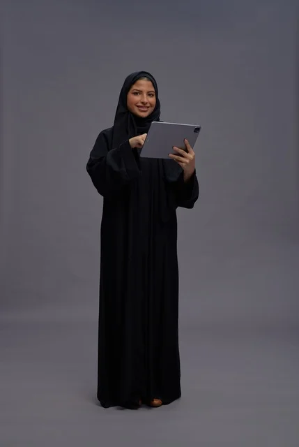 امرأة سعودية بالعباءة السوداء تستخدم جهازاً لوحياً