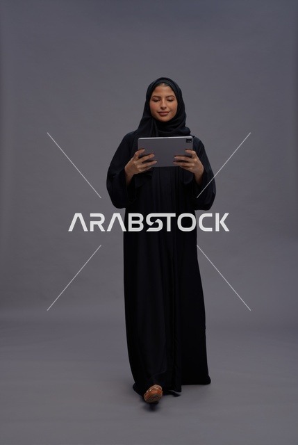 امرأة سعودية بعباءة سوداء تستخدم جهازاً لوحياً