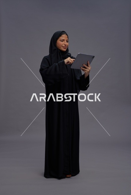 امرأة سعودية بالعباءة السوداء تستخدم جهازاً لوحياً