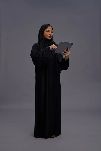 امرأة سعودية بالعباءة السوداء تستخدم جهازاً لوحياً