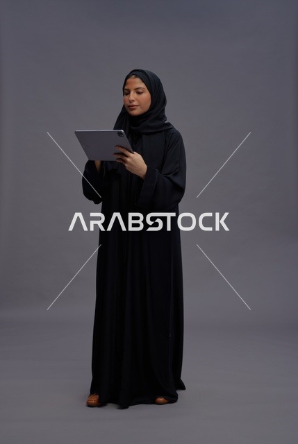 امرأة سعودية تستخدم جهازاً لوحياً بالعباءة السوداء