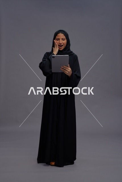 امرأة سعودية تستخدم جهازاً لوحياً بتعبيرات مندهشة