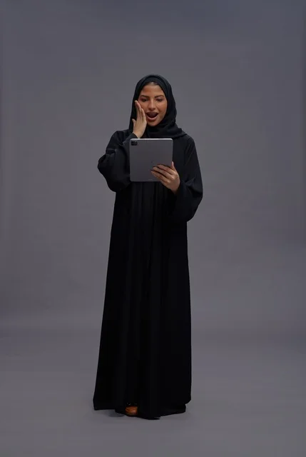 امرأة سعودية تستخدم جهازاً لوحياً بتعبيرات مندهشة