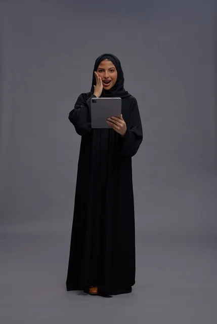 امرأة سعودية تحمل جهازا لوحيا بتعبير مندهش