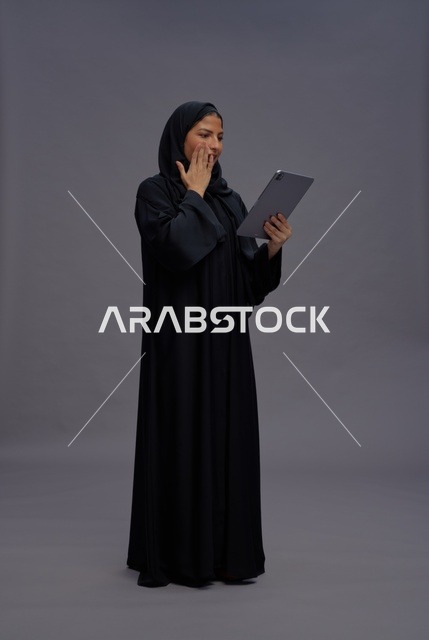 امرأة سعودية تحمل جهازاً لوحياً بتعبير مندهش