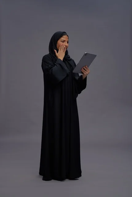 امرأة سعودية تحمل جهازاً لوحياً بتعبير مندهش