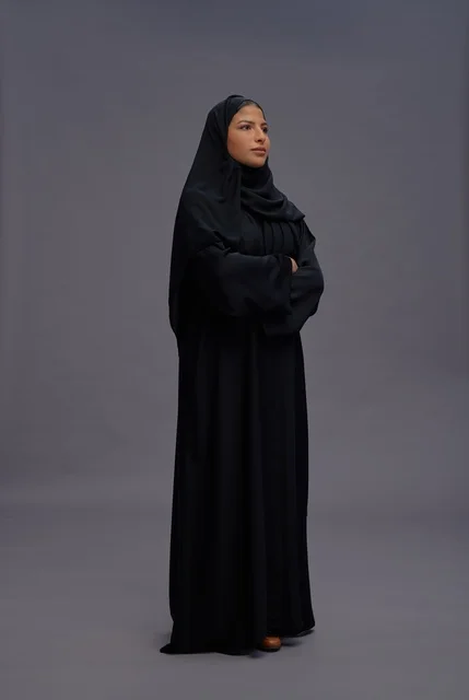 امرأة سعودية بعباءة سوداء بوضعية واثقة في الاستوديو