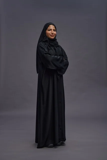 امرأة سعودية بعباءة سوداء تقف بذراعين متقاطعتين