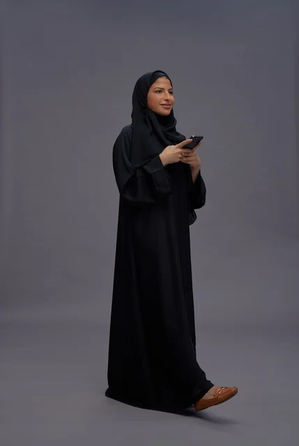 امرأة سعودية بالعباءة تستخدم الهاتف الذكي في الاستوديو