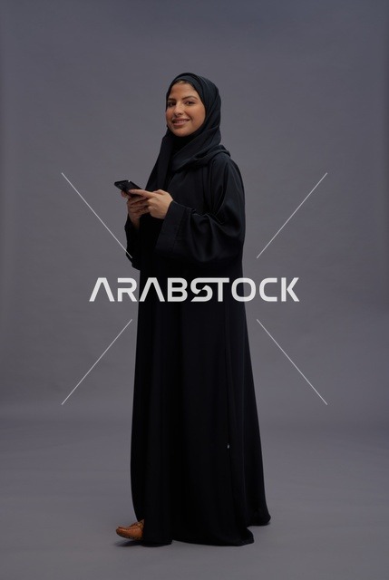 امرأة سعودية بالعباءة السوداء تستخدم الهاتف الذكي