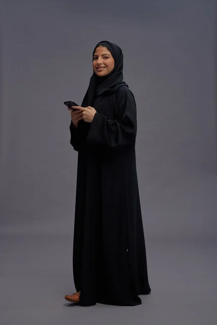 امرأة سعودية بالعباءة السوداء تستخدم الهاتف الذكي