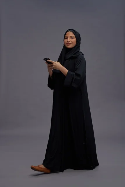 Saudi Woman in Abaya Using Smartphone on Grey Background