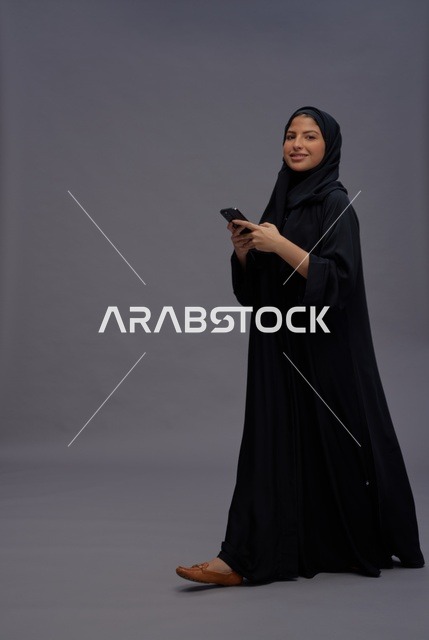 امرأة سعودية بالعباءة تستخدم الهاتف الذكي في استوديو