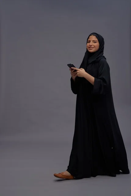 امرأة سعودية بالعباءة تستخدم الهاتف الذكي في استوديو